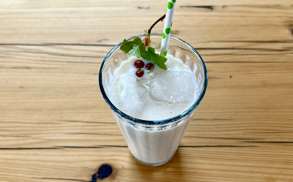 KI generiert: Ein Glas Milchshake mit Eiswürfeln, rotem Beerenzweig und grünem Strohhalm auf Holztisch.