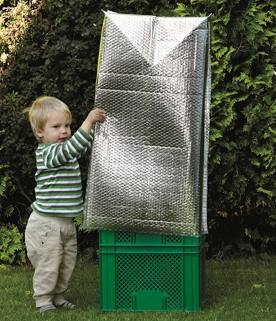 KI generiert: Ein Kind spielt im Garten mit einer grünen Kiste, die mit einer reflektierenden Folie bedeckt ist.