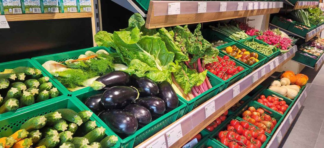 KI generiert: Frisches Gemüse in einem Ladenregal: Zucchini, Auberginen, Blattgemüse, Tomaten und mehr.