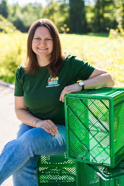 KI generiert: Eine Person sitzt lächelnd auf grünen Plastikkisten im Freien. Text auf Shirt: "Ökokiste Biokiste."