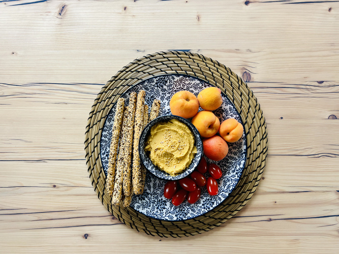 KI generiert: Teller mit Grissini, Hummus, Aprikosen und Kirschtomaten auf einem Holztisch.