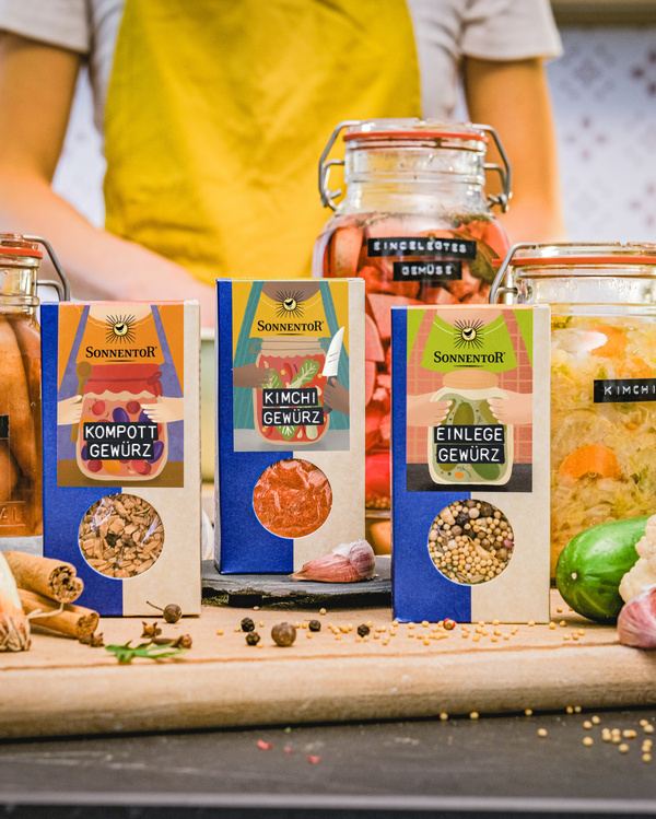 KI generiert: Gewürzpackungen und Einmachgläser auf einem Tisch, Person im Hintergrund. Text: "SONNENTOR Kompott Gewürz, Kimchi Gewürz, Einlege Gewürz".