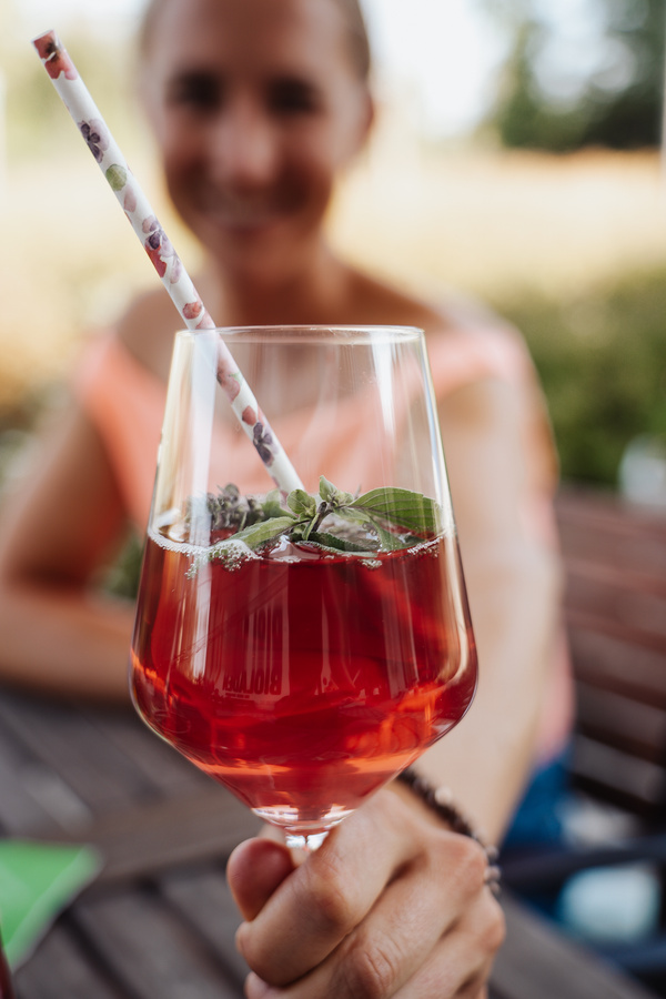 KI generiert: Ein Glas rotes Getränk mit Strohhalm und Kräutern wird von einer Person dargeboten.