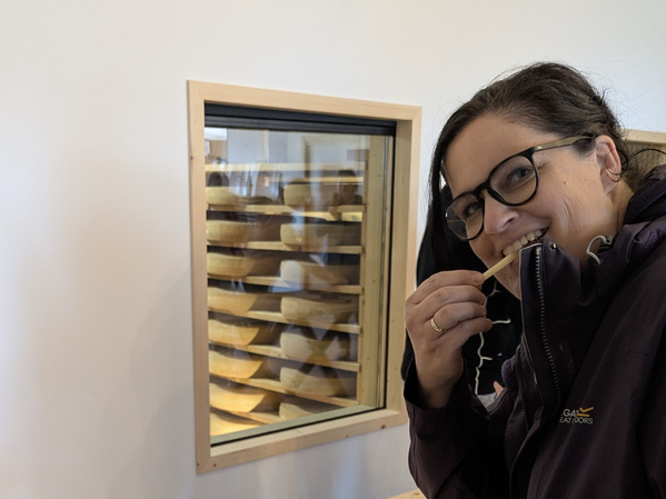 KI generiert: Eine Frau probiert Käse, im Hintergrund ein Fenster mit Käselaiben.