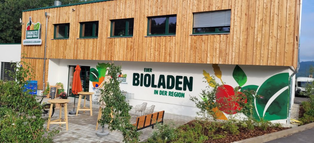 KI generiert: Holzgebäude mit Terrasse, Außenbereich und dem Text: "EUER BIOLADEN IN DER REGION".