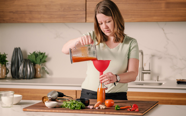 KI generiert: Eine Frau füllt Saucen mit einem Trichter in Flaschen in einer Küche ab.
