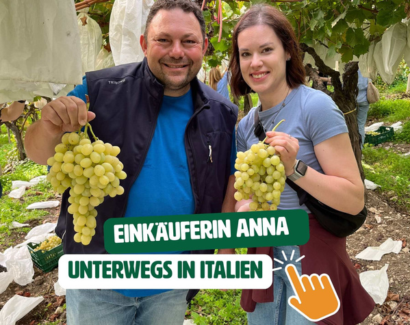 KI generiert: Zwei Personen halten Trauben. Text: "Einkäuferin Anna unterwegs in Italien".