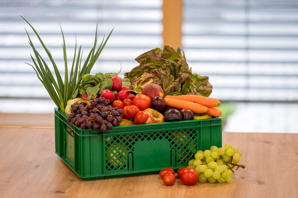 KI generiert: Das Bild zeigt zwei Personen hinter einem Tisch, der mit einer Vielzahl von frischem Obst und Gemüse bedeckt ist. Es gibt ein Werbeschild, das darauf hinweist, dass die sechste Kiste kostenlos ist.