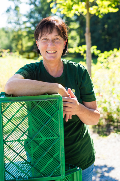 KI generiert: Frau in grünem Shirt lächelt, lehnt an grüner Kiste im Freien.