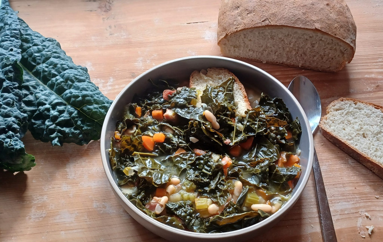 Toskanische Gemüsesuppe mit frischem Brot und Palmkohlblättern auf einem Holztisch