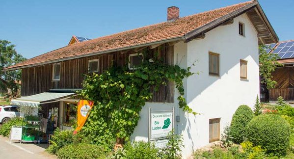KI generiert: Ein Bio-Laden in einem traditionellen Gebäude, umgeben von Pflanzen. Text: "Ökokiste Kößnach Bio Laden".