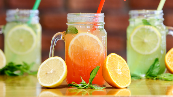 KI generiert: Erfrischende Getränke in Gläsern mit Zitronenscheiben und Minze, rote und grüne Farben, auf einem Holztisch.