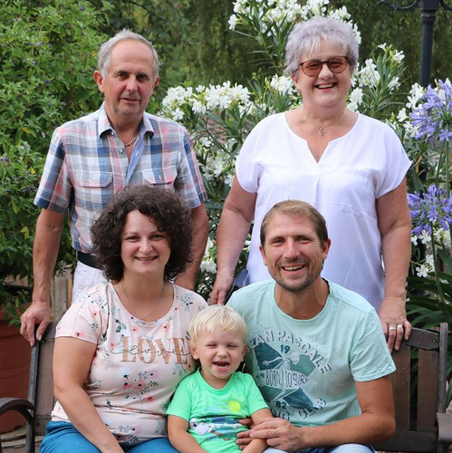 KI generiert: Familienfoto mit fünf Personen, im Freien aufgenommen. Im Hintergrund sind blühende Pflanzen zu sehen.