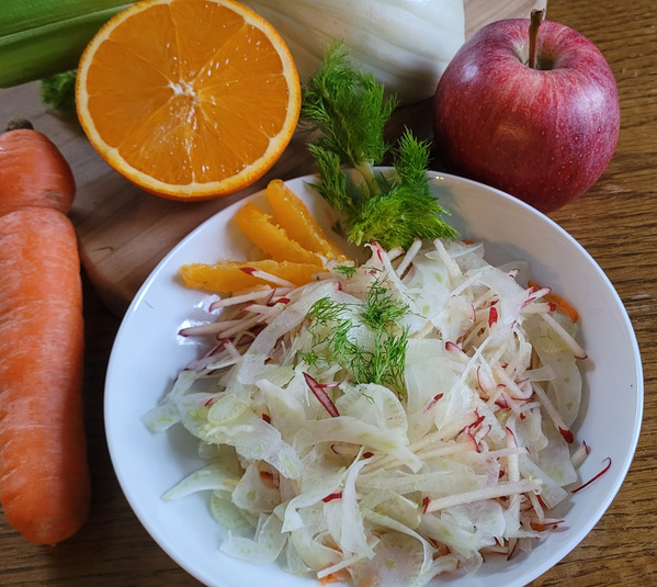 KI generiert: Ein Teller mit Fenchelsalat, umgeben von Karotte, Orange, Apfel und Fenchel auf einem Holzbrett.
