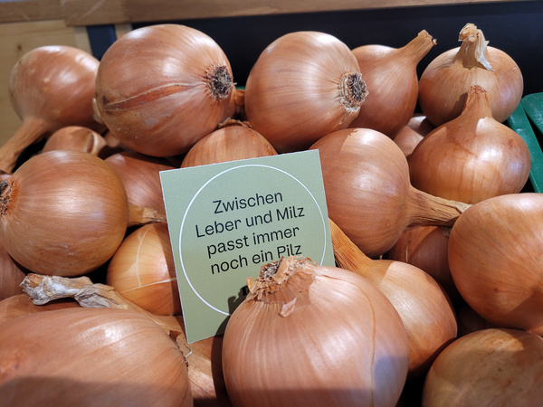 KI generiert: Ein Haufen Zwiebeln mit einem Schild: "Zwischen Leber und Milz passt immer noch ein Pilz".