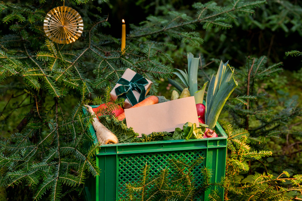 KI generiert: Grüne Kiste mit Gemüse und Geschenk, dekoriert mit Zweigen, Kerze und Ornament.