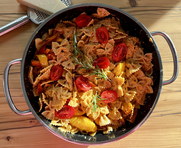 KI generiert: Farfalle-Pasta mit Kirschtomaten und Rosmarin in einer Pfanne auf einem Holztisch.