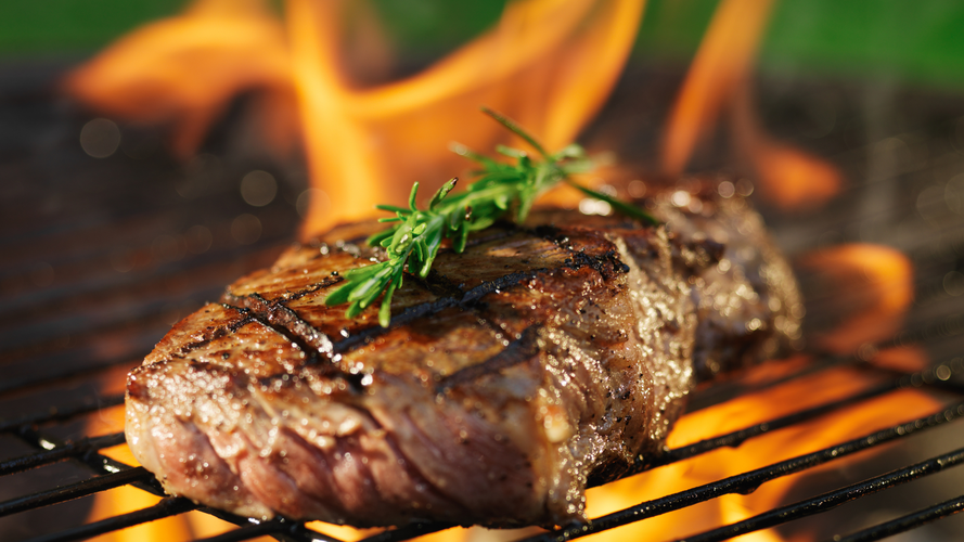 KI generiert: Ein saftiges Steak mit Rosmarin wird auf einem Grill über offenem Feuer zubereitet.
