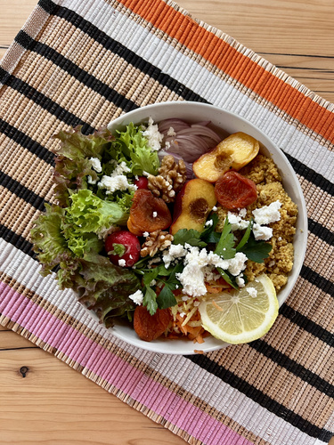 KI generiert: Eine bunte Bowl mit Salat, Couscous, Nüssen und Feta auf einer gestreiften Unterlage.