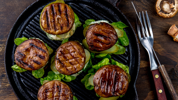 KI generiert: Gegrillte Pilze auf Salat auf einer Grillpfanne, daneben Messer und Gabel.