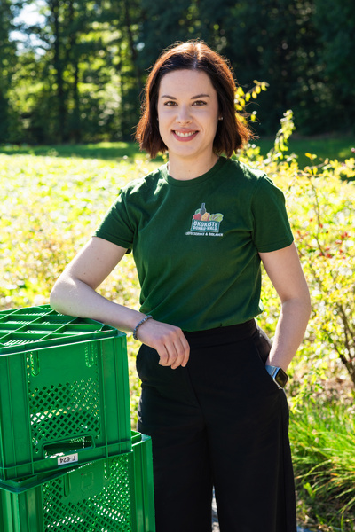 KI generiert: Eine Person in grüner Kleidung steht neben grünen Kisten, im Hintergrund Natur. Text: "Ökokiste".