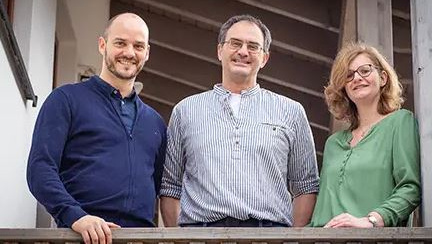 KI generiert: Drei Personen stehen lächelnd auf einem Balkon.