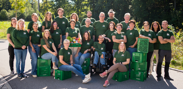 KI generiert: Eine Gruppe von Menschen posiert draußen in grünen T-Shirts, teils mit grünen Kisten.