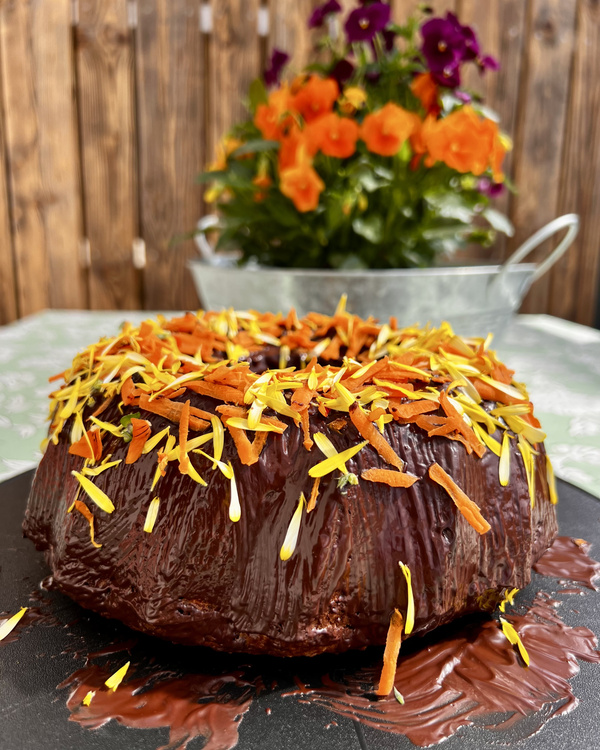 KI generiert: Ein Schokoladenkuchen mit bunter Blütendekoration, im Hintergrund ein Blumenarrangement.