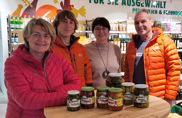 KI generiert: Eine Gruppe von vier Personen steht hinter einem Tisch mit eingelegtem Gemüse. Text: "FÜR SIE AUSGEWÄHLT".