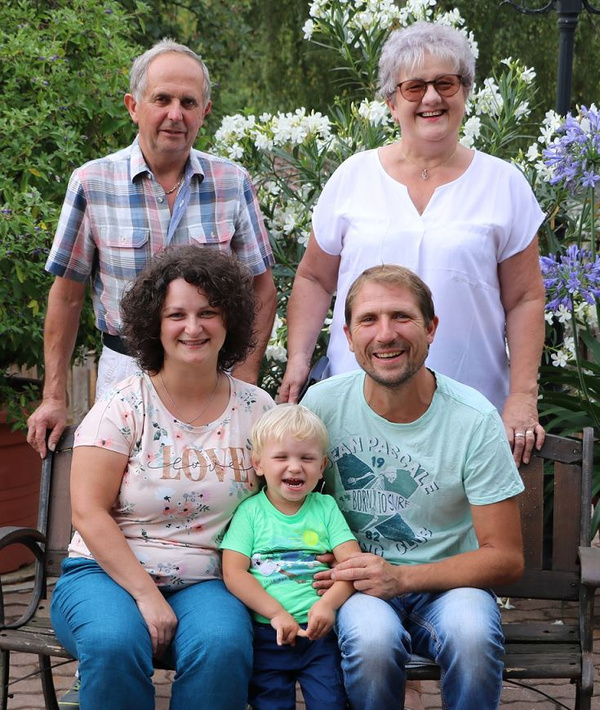 KI generiert: Eine lächelnde Familie posiert auf einer Bank im Garten.