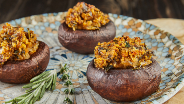 KI generiert: Drei gefüllte Champignons auf einem gemusterten Teller mit Rosmarinzweig dekoriert.