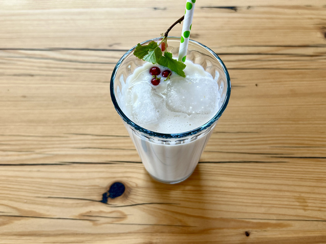 KI generiert: Ein Glas Milchshake mit Eiswürfeln, Trinkhalm und Beerenzweig auf einem Holzuntergrund.