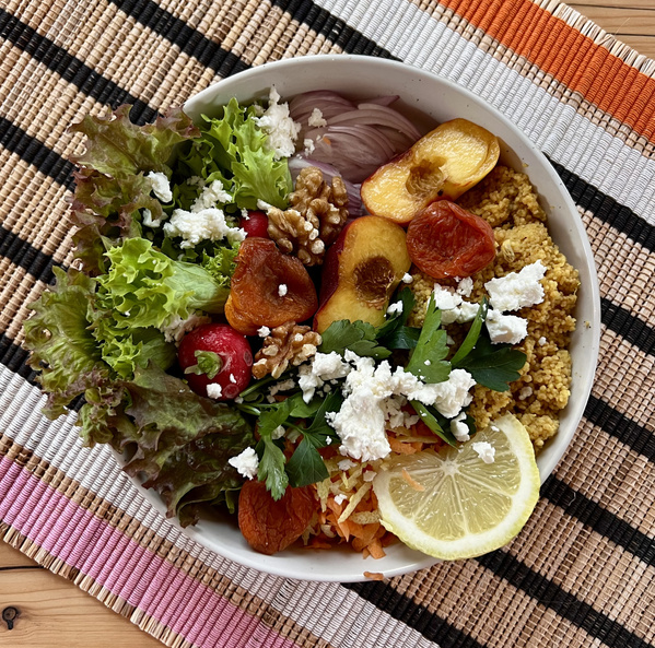 KI generiert: Bunte Buddha-Bowl mit frischem Salat, Hülsenfrüchten, Feta, Nüssen und Zitrone auf einem Tischset.