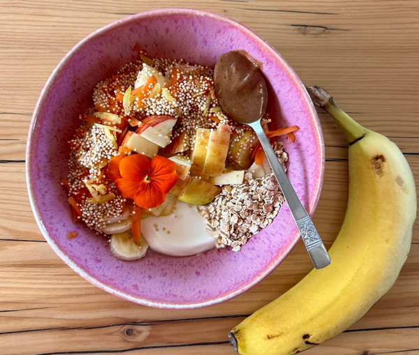 KI generiert: Schüssel mit Obst, Quinoa, Haferflocken, Joghurt, Blüte und Nussmus; daneben liegt eine Banane.