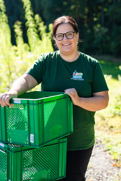 KI generiert: Eine Person in grünem T-Shirt mit Ökokiste-Logo hält grüne Kisten draußen in der Natur.