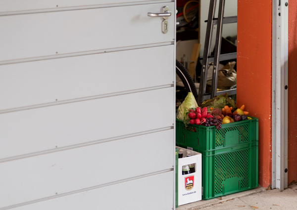 KI generiert: Eine halb geöffnete Tür zeigt Kisten mit frischem Obst und Gemüse. Text: "www.hoefler.de".