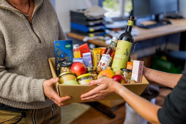 KI generiert: Zwei Personen übergeben einen Präsentkorb mit Lebensmitteln und Getränken.