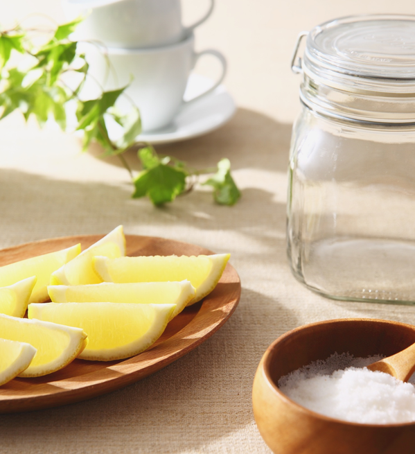 KI generiert: Ein Teller mit Zitronenspalten, ein Glasgefäß und eine Schale mit Salz auf einem Tisch.
