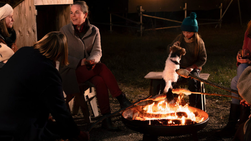 KI generiert: Personen sitzen abends um ein Lagerfeuer im Freien.