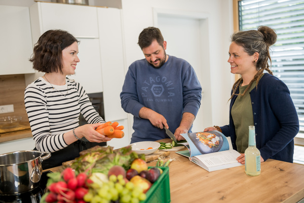 KI generiert: Drei Personen kochen gemeinsam in einer Küche mit frischem Obst und Gemüse.