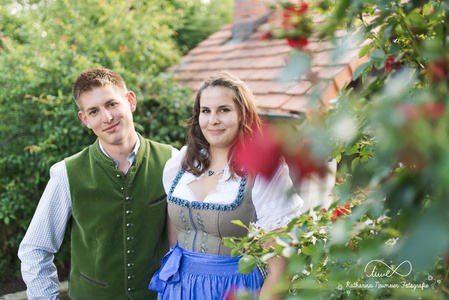 KI generiert: Zwei Personen stehen an einer gemauerten Brüstung und lächeln, während im Hintergrund eine weite Landschaft mit einem Berg sichtbar ist. Das Bild scheint an einem sonnigen Tag aufgenommen worden zu sein.