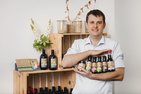 KI generiert: Ein Mann steht lächelnd vor einem Regal mit verschiedenen Flaschen und Produkten, während er weitere Flaschen in seinen Armen hält. Das Bild vermittelt den Eindruck eines Geschäfts oder einer Produktpräsentation.