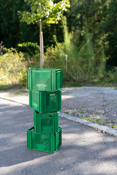 KI generiert: Ein Stapel grüner Plastikkisten steht draußen auf einem Weg.