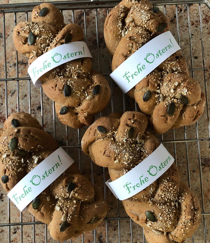 KI generiert: Geflochtene Brote mit Kernen, verziert mit "Frohe Ostern!"-Banderolen auf einem Gitter.