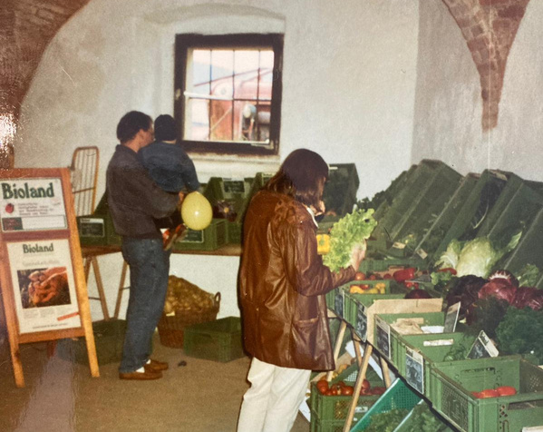 KI generiert: Leute kaufen Biogemüse in einem Laden. Ein Schild zeigt "Bioland".
