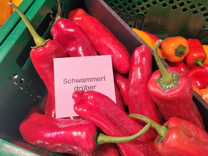 KI generiert: Rote Paprikaschoten in einem Korb, mit einem Schild: "Schwammerl drüber".
