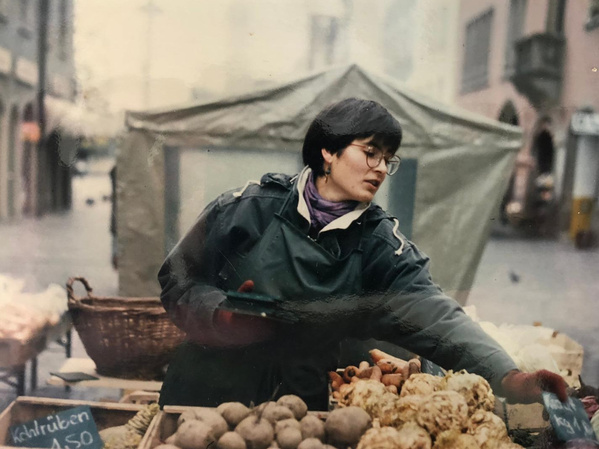 KI generiert: Eine Person verkauft Gemüse auf einem Markt. Text: "Kohlrüben 1,50".