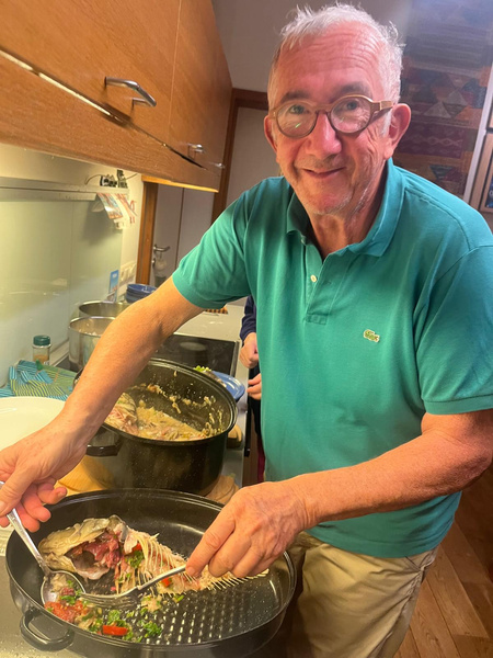 KI generiert: Ein Mann in einem türkisfarbenen Poloshirt bereitet in einer Küche ein Fischgericht zu. Er lächelt in die Kamera, während er den Fisch mit einer Gabel in der Pfanne hält.