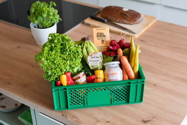 KI generiert: Eine grüne Kiste mit frischem Obst, Gemüse und fairen Produkten auf einem Küchentisch.